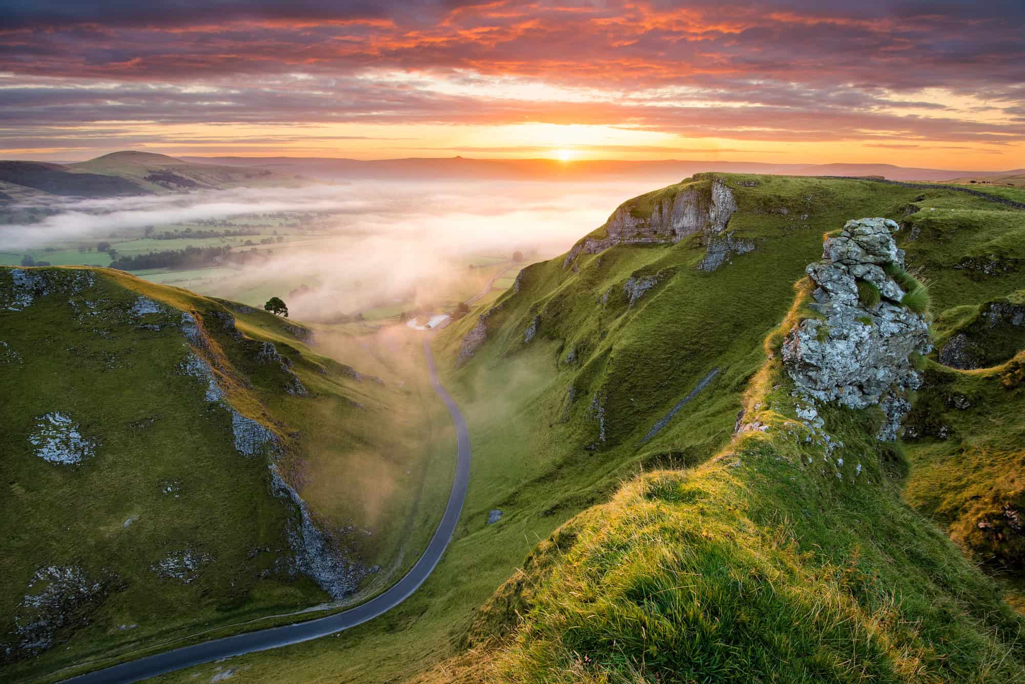 Long winding rural road leading into misty valley in the English Peak District