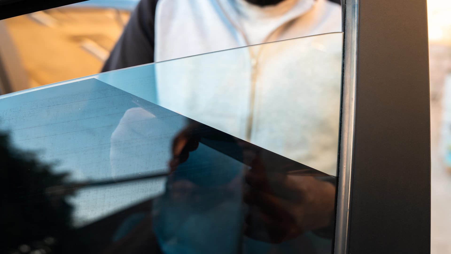 A man removes the tint from the side windows of a car