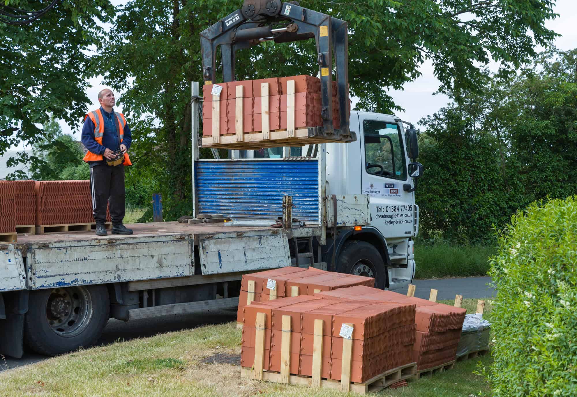 Man delivering building materials (roof tiles), delivery lorry with crane, UK
