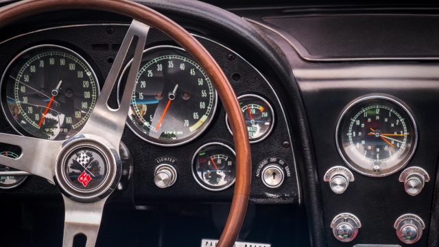 TORONTO, CANADA - 08 18 2018: Steering wheel with flags logo on horn button, speedometer, revs, fuel and battery dials, gear lever, buttons and knobs on the front panel of blue 1966 Chevrolet Corvette — Photo by vadim.rodnev
