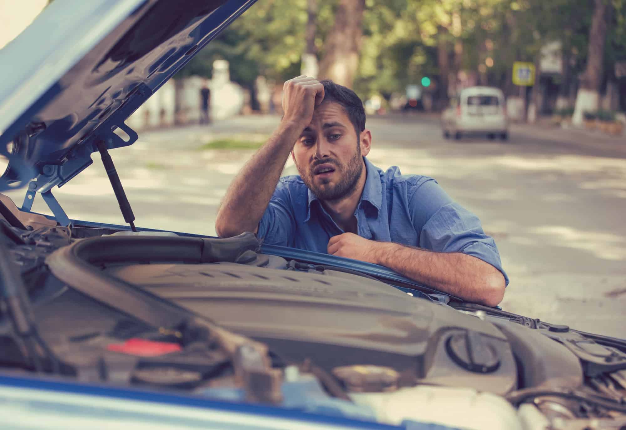 Stressed man having trouble with broken car looking in frustration at failed engine