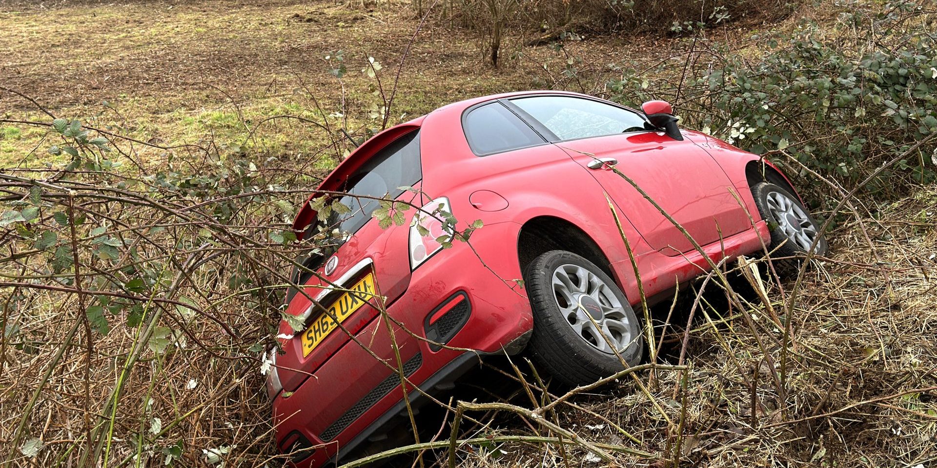 Pontyclun, Wales, UK - 29 January 2025: Small red car on its side in bushes after crashing off a road — Photo by CeriBreeze