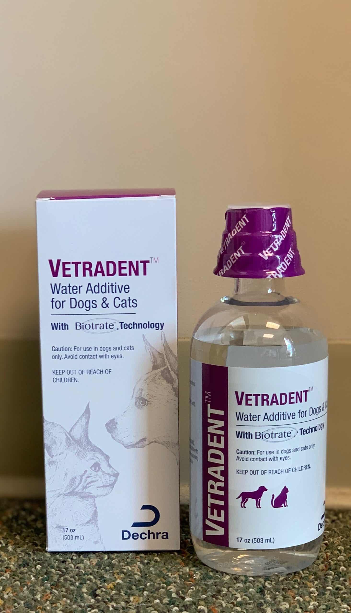 A bottle of veterinarian-approved vetraderm water additive for dogs next to its packaging box, featuring the brand logos and pet illustrations, placed on a speckled gray surface against a beige wall.