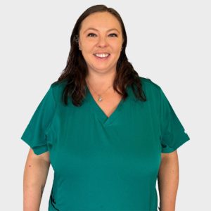 A woman with long, dark hair and a friendly smile, wearing a teal veterinary scrub top, standing against a plain white background.