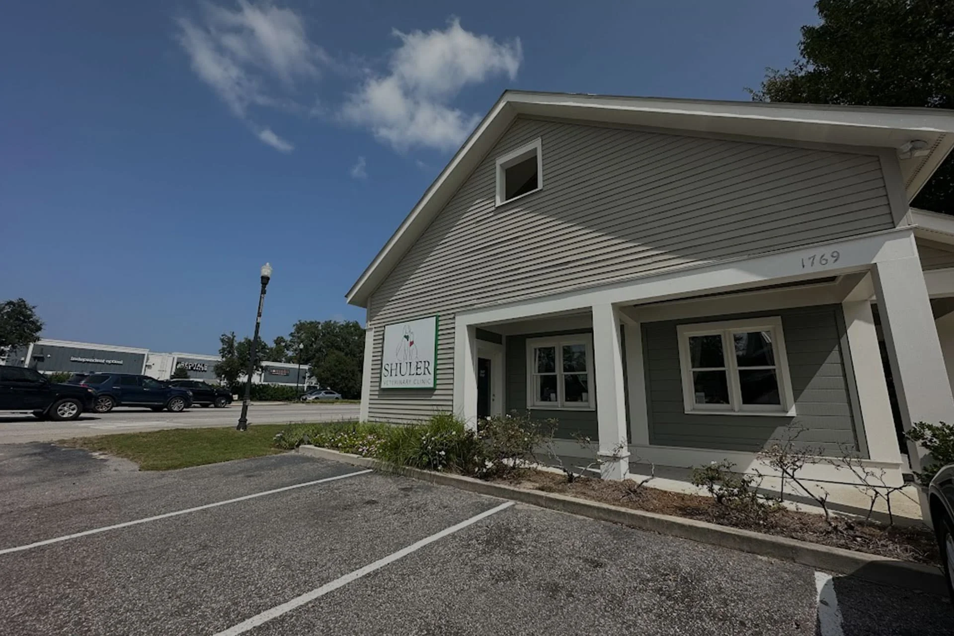 A white single-story suburban commercial building with a sign that reads "fitzler veterinarian." A parking lot in the foreground and trees under a blue sky.