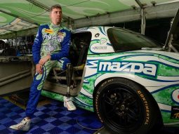 A man receiving manual therapy next to a Mazda race car.