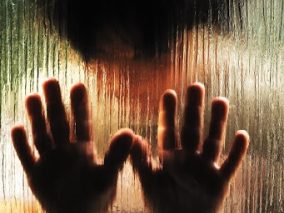 A person's hands practicing manual therapy are seen through a glass window, promoting recovery and health and wellness.