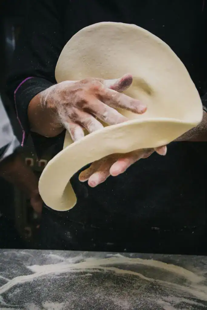 Close-up of chef tossing pizza dough in a kitchen, showcasing expert culinary skills.
