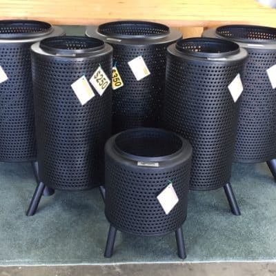 Black perforated metal trash cans with angled legs for modern waste disposal.