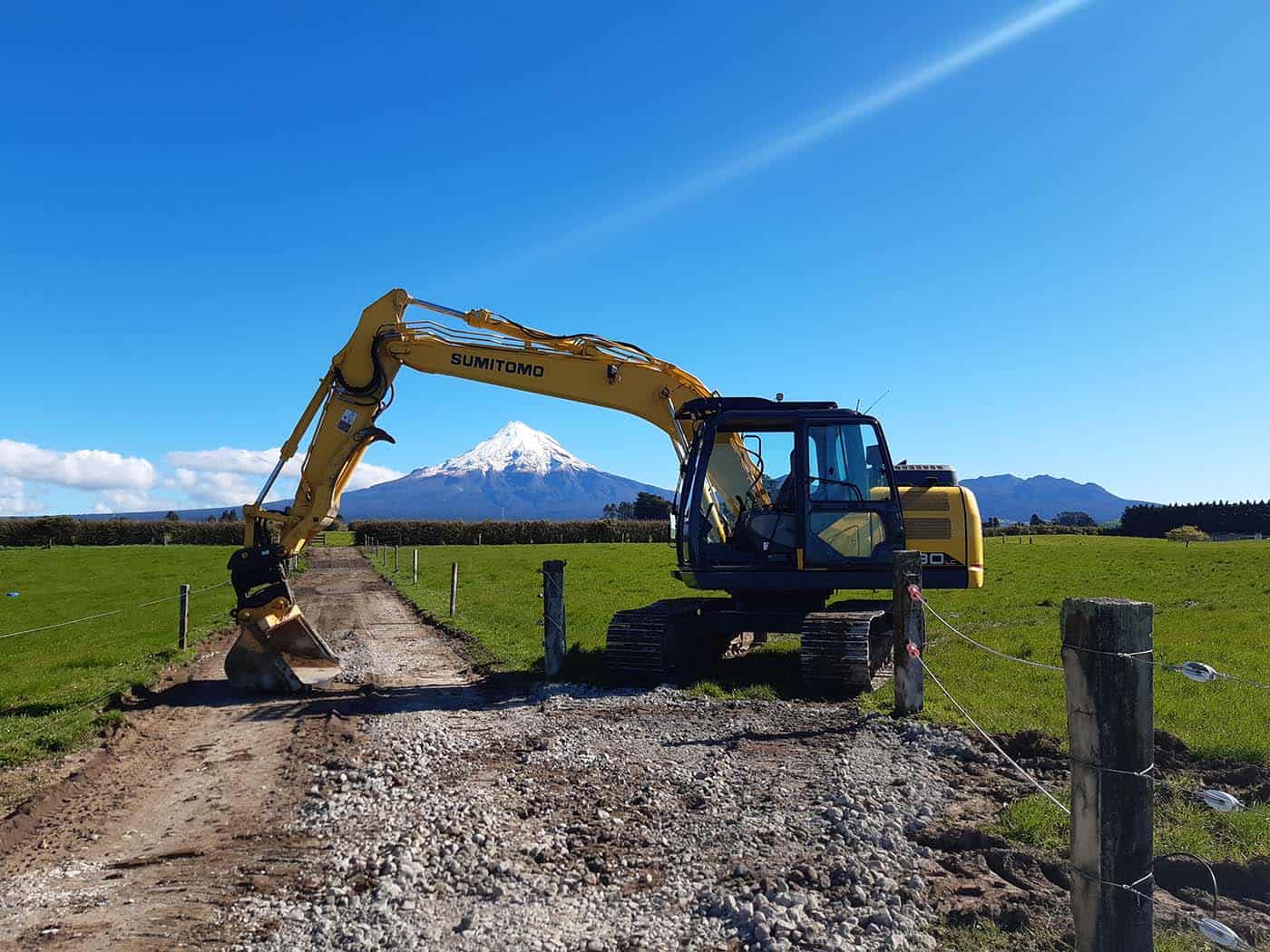Heavy construction excavator working on a rural dirt path with Mount Taranaki in the background.