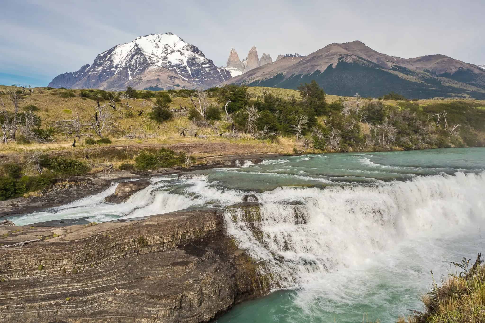 Cascada en Torres del Paine con montañas nevadas al fondo, excursión desde El Calafate