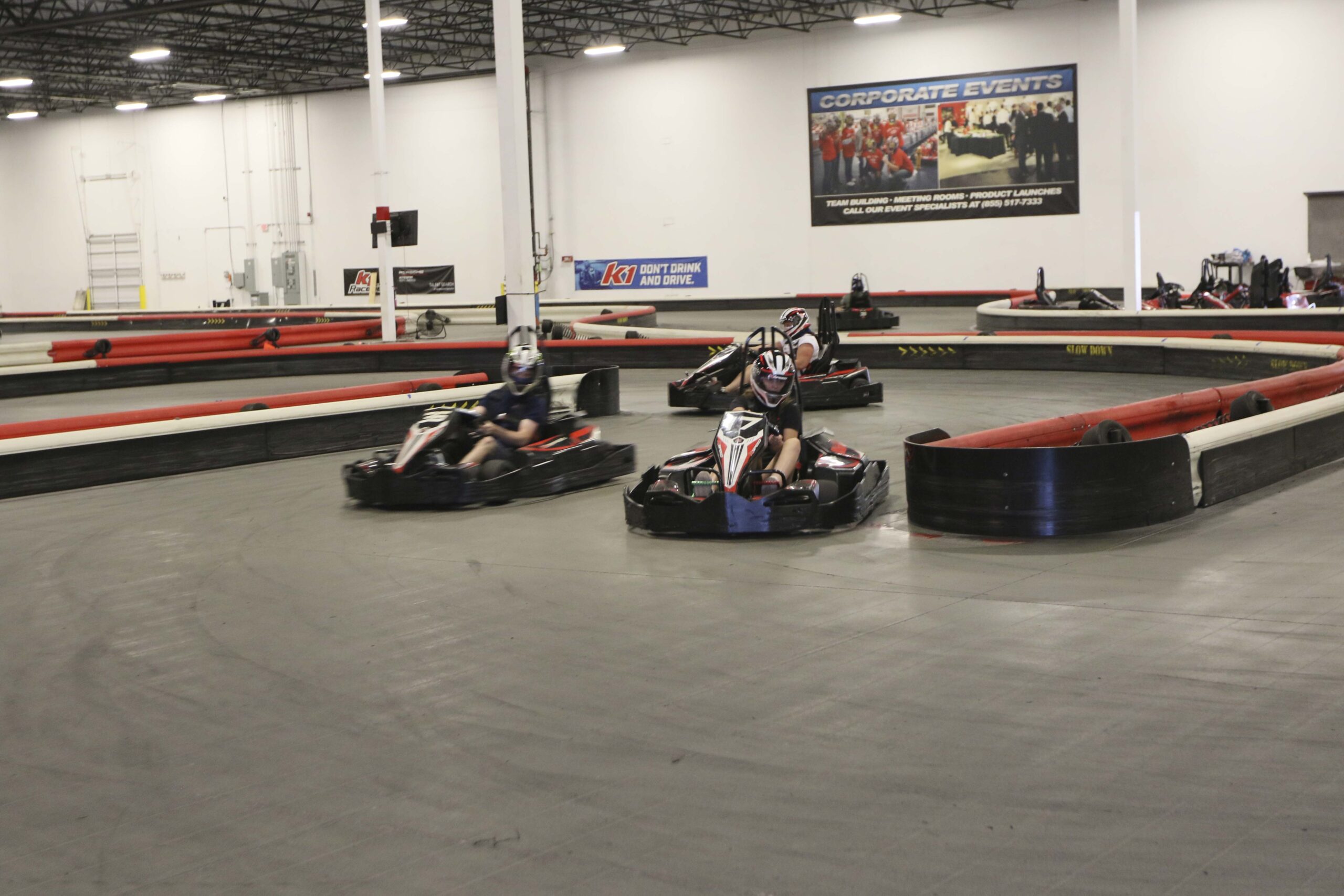 Indoor go-kart racing track with drivers in action at Mustang Week event.