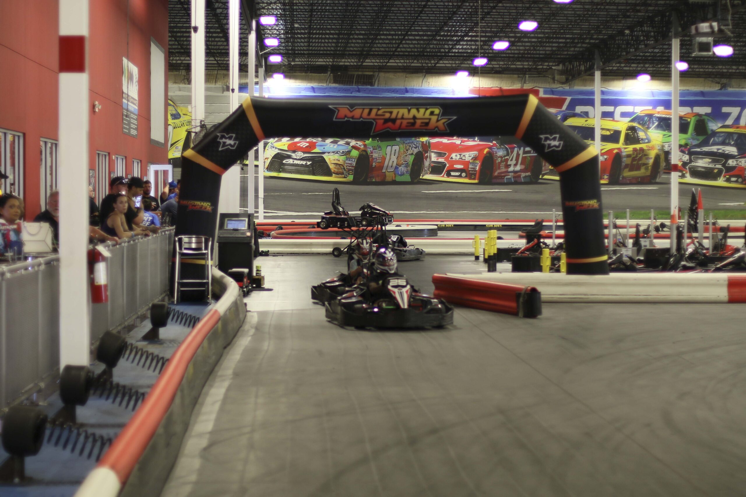 Indoor go-kart racing track with cars and spectators at Mustang Week event.