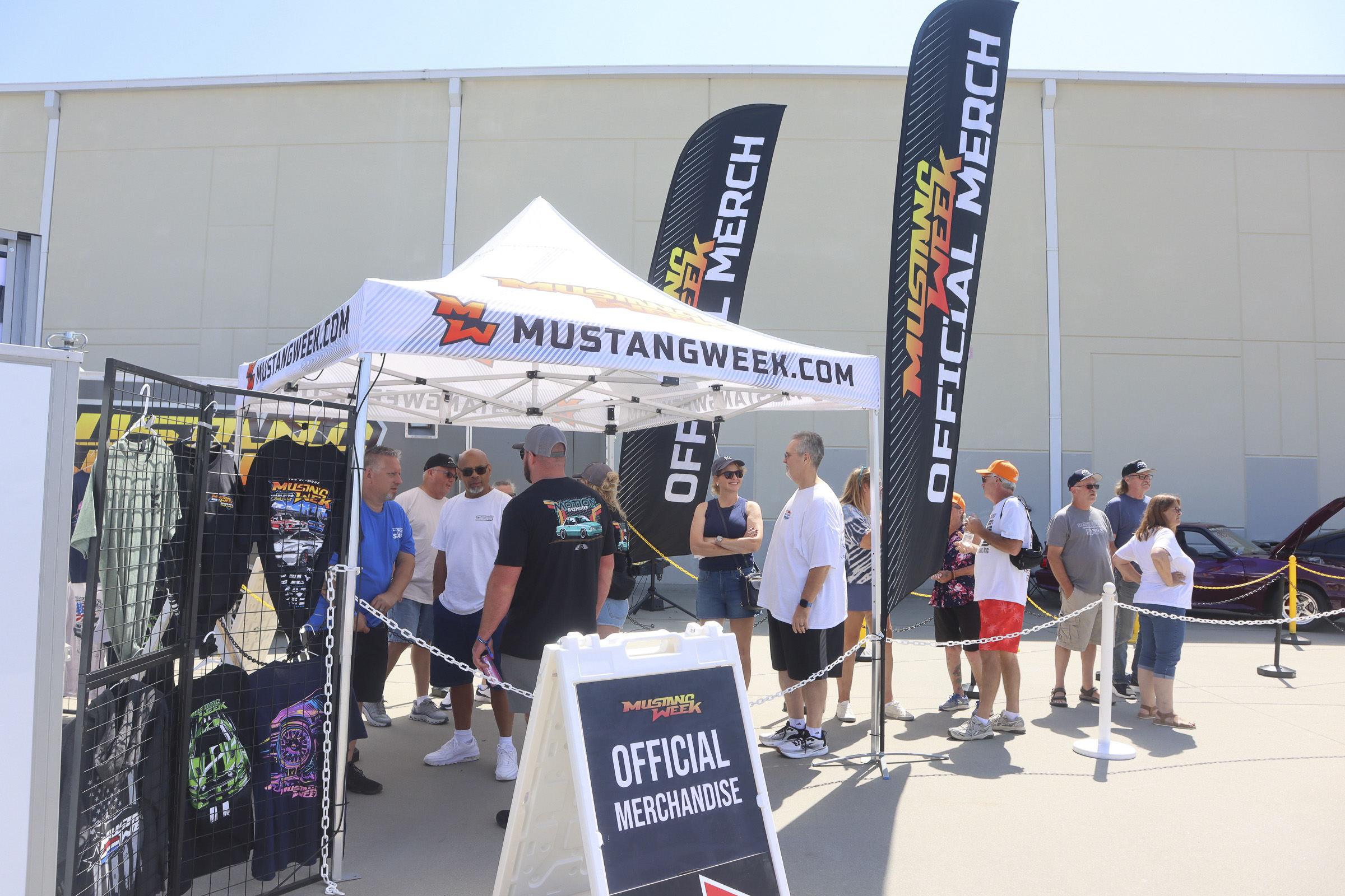 People at Mustang Week merchandise booth with flags and T-shirts.