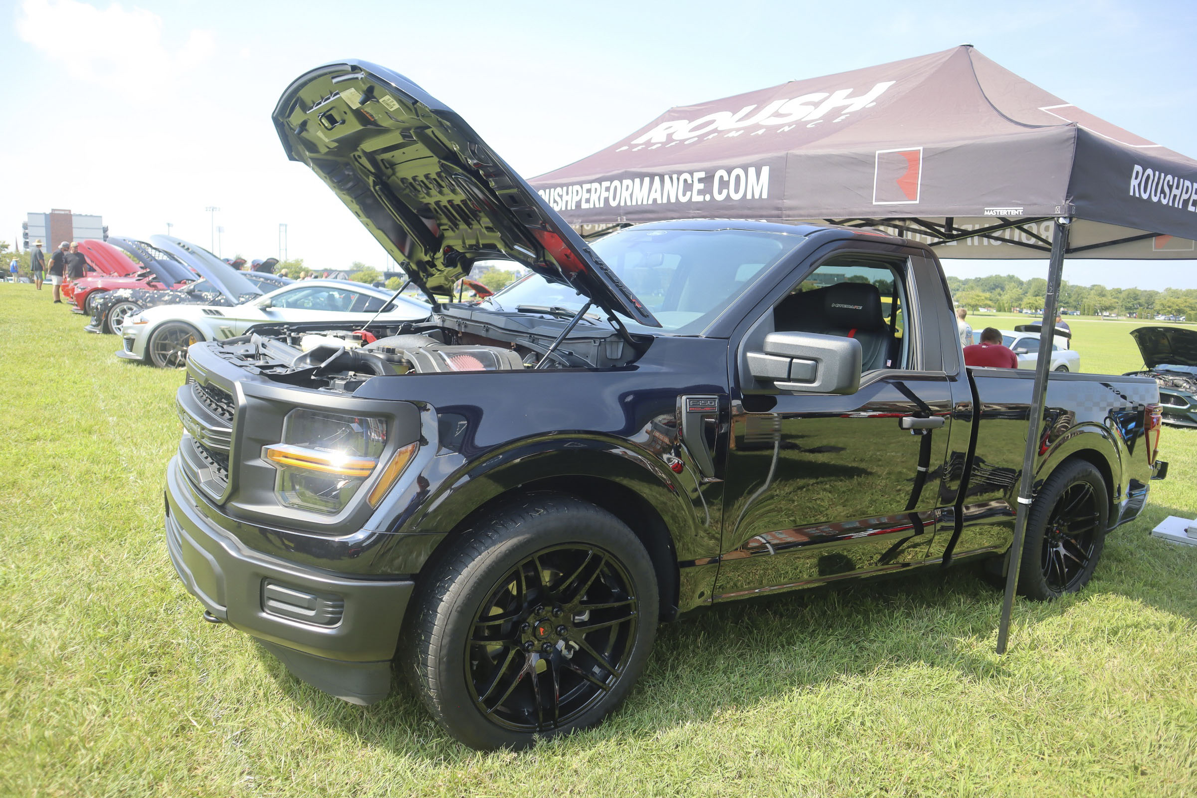 Black Ford truck with open hood at Mustang Week event in Charlotte.