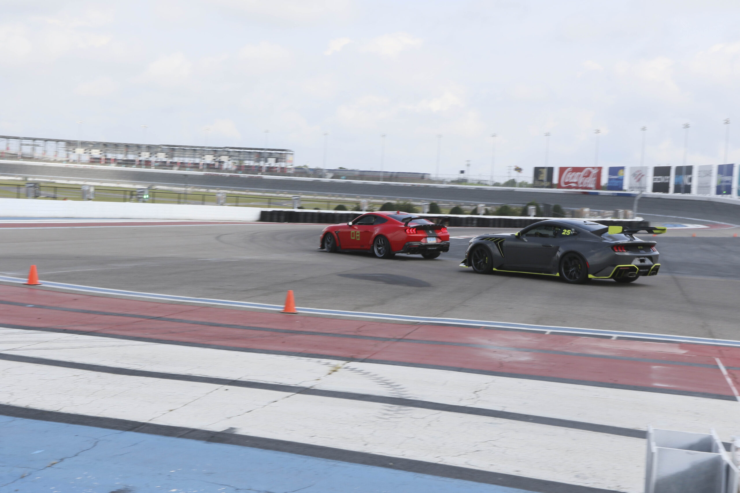 Two high-performance sports cars racing on a track during Mustang Week event.