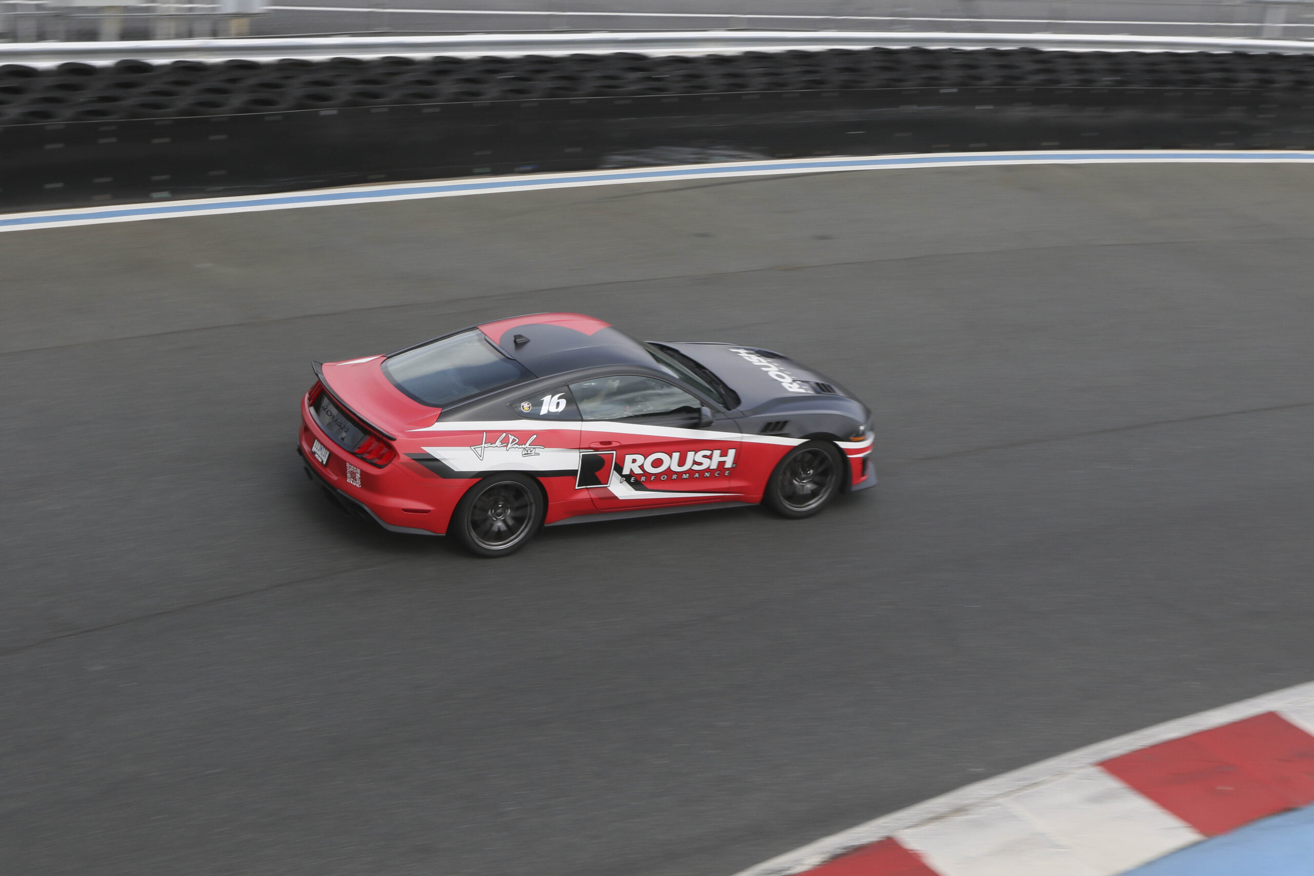 Red and black Mustang race car on the racetrack during Mustang Week event.