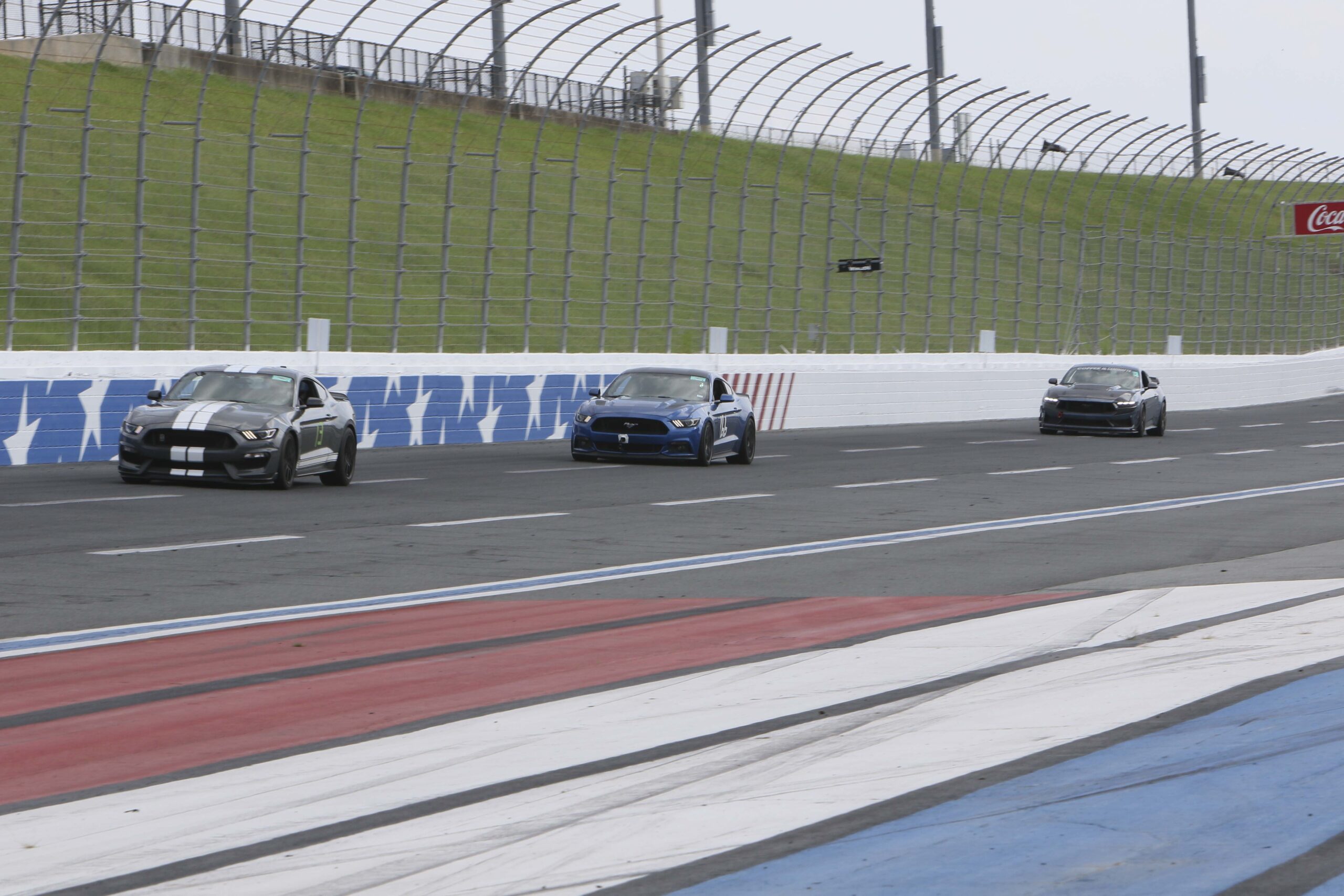 High-speed Ford Mustangs racing on Charlotte Motor Speedway track.