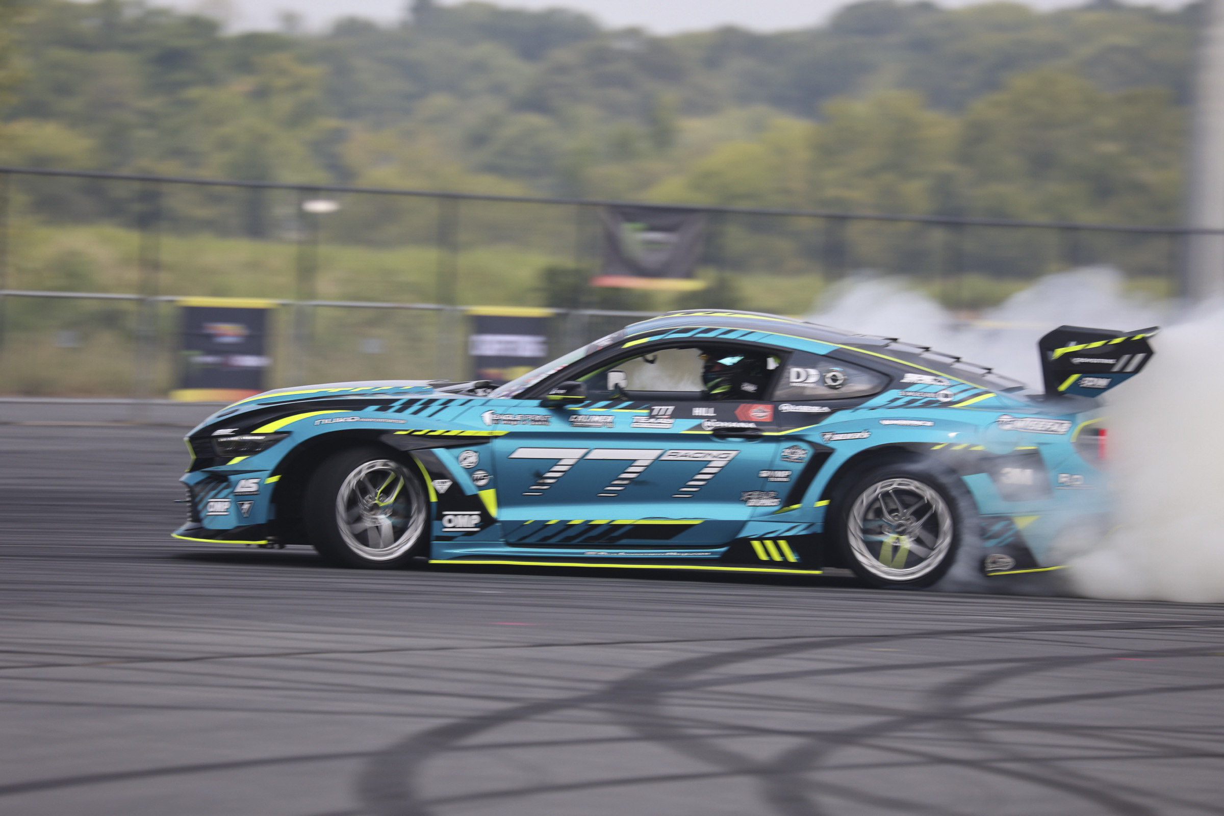Blue Mustang race car drifting at Mustang Week event.