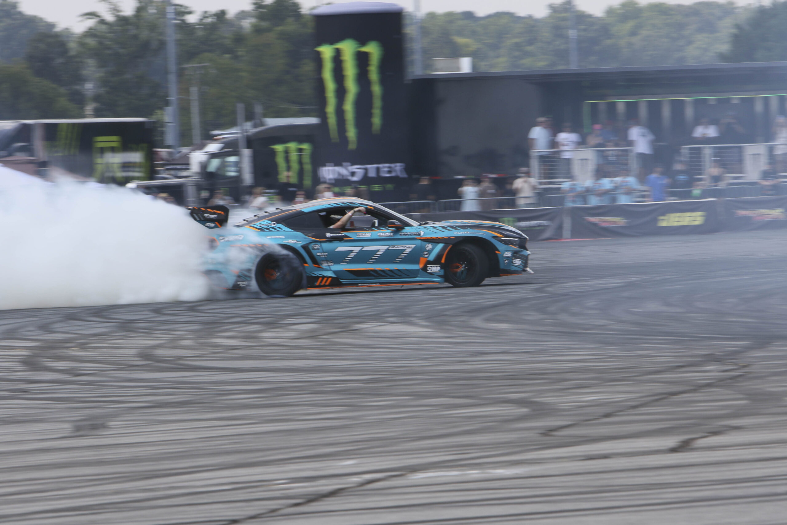 Blue Ford Mustang drifting with smoke at Mustang Week event.