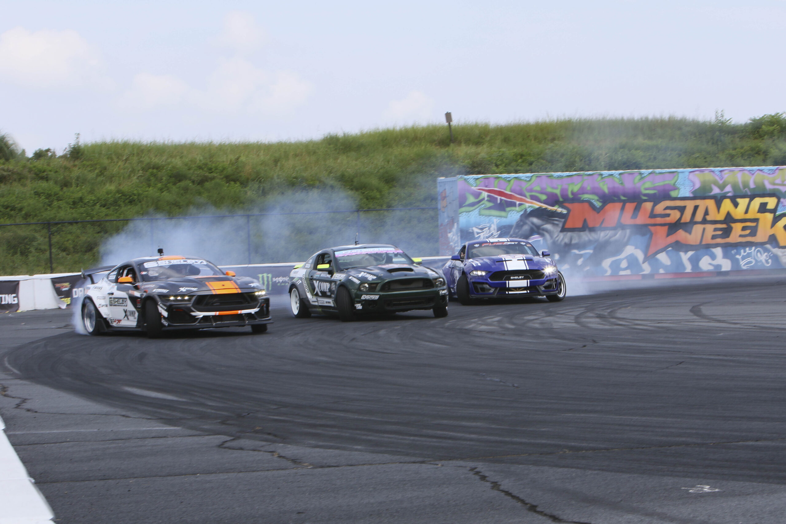 Three Ford Mustangs drifting on a race track at Mustang Week event.