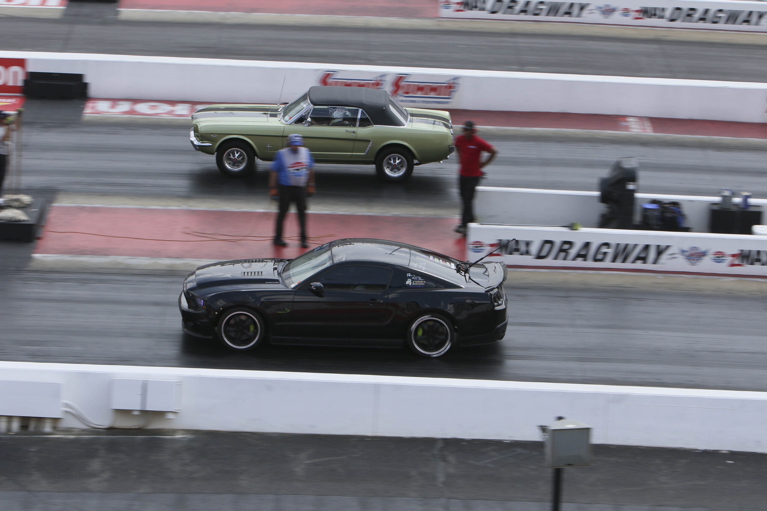 Black sports car racing on drag strip during Mustang Week event.
