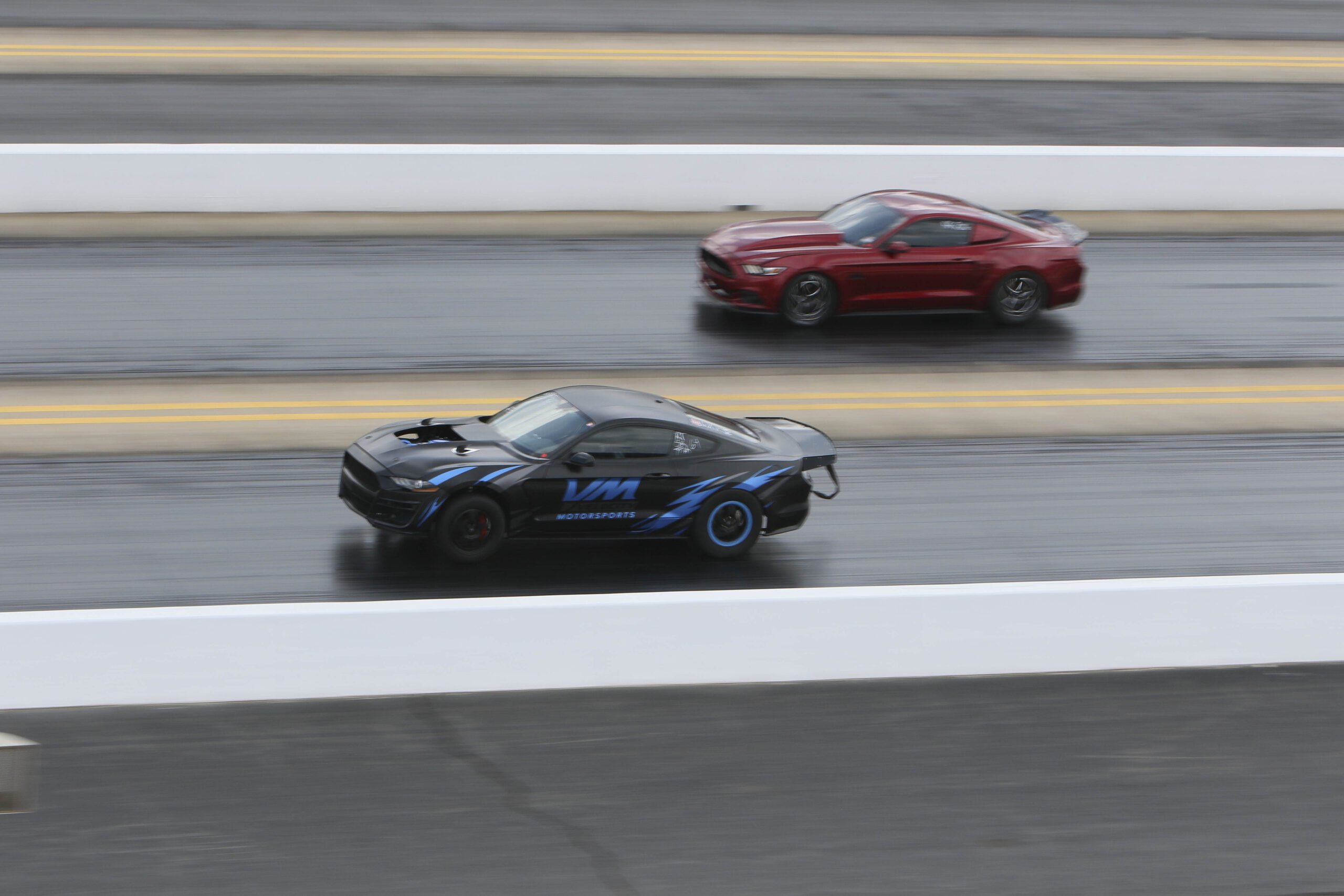 Two sports cars racing on a drag strip during Mustang Week event.