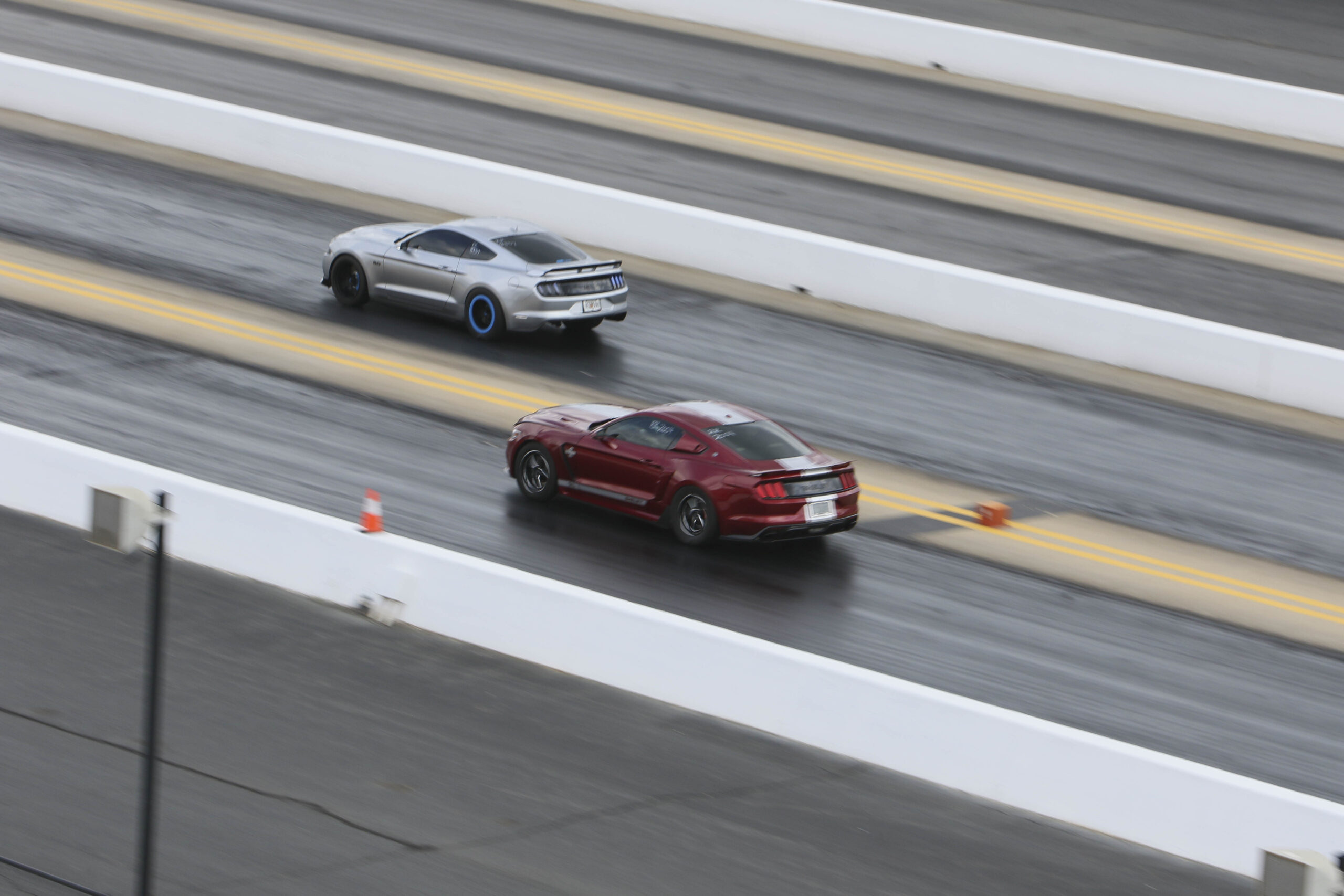 Two Mustang cars racing on a drag strip during Mustang Week event.