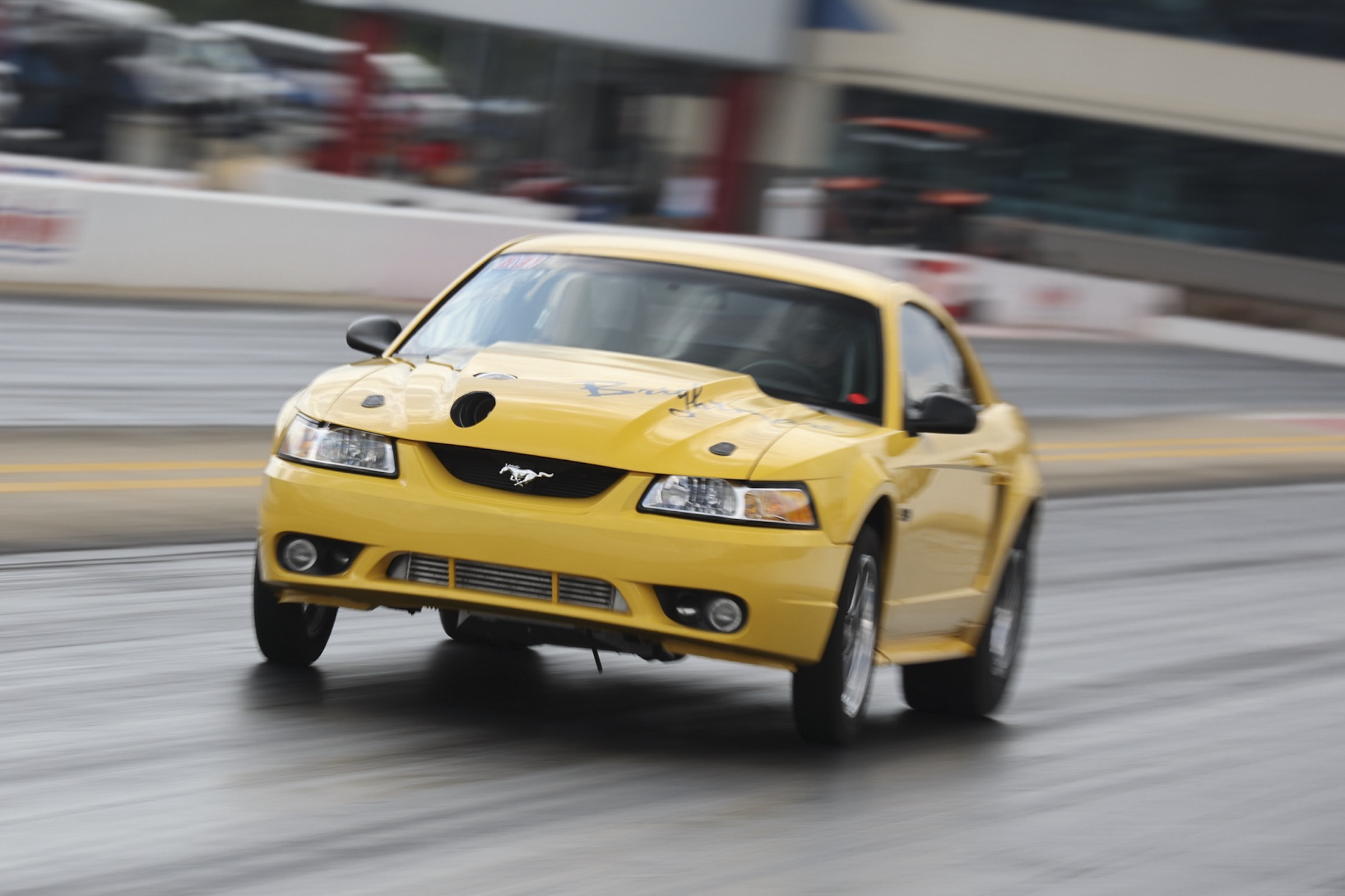 Yellow Ford Mustang racing car on track at Mustang Week event.
