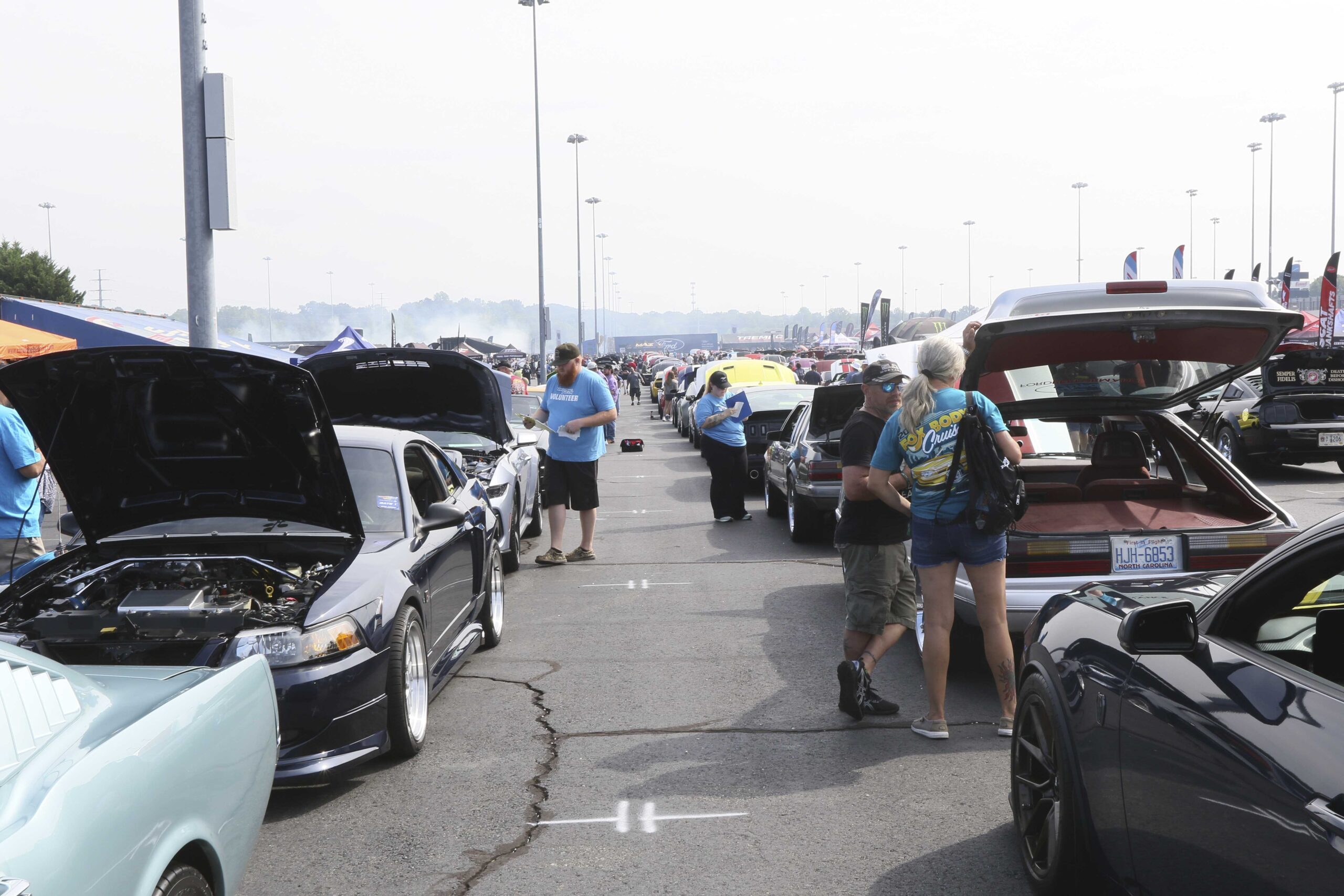 People viewing and discussing classic and modern Ford Mustangs at Mustang Week event.