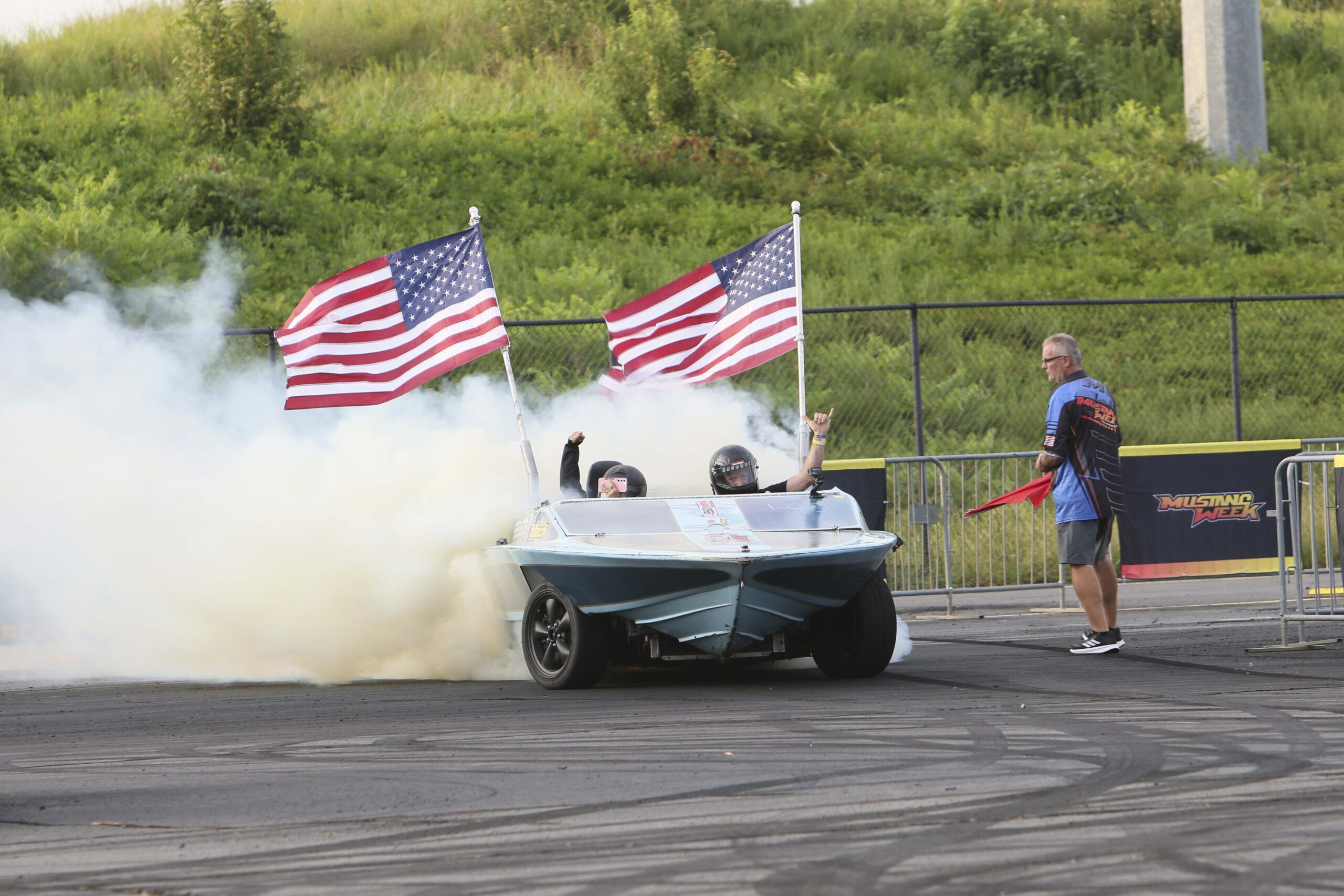 High-speed drag racing car with American flags at Mustang Week event.