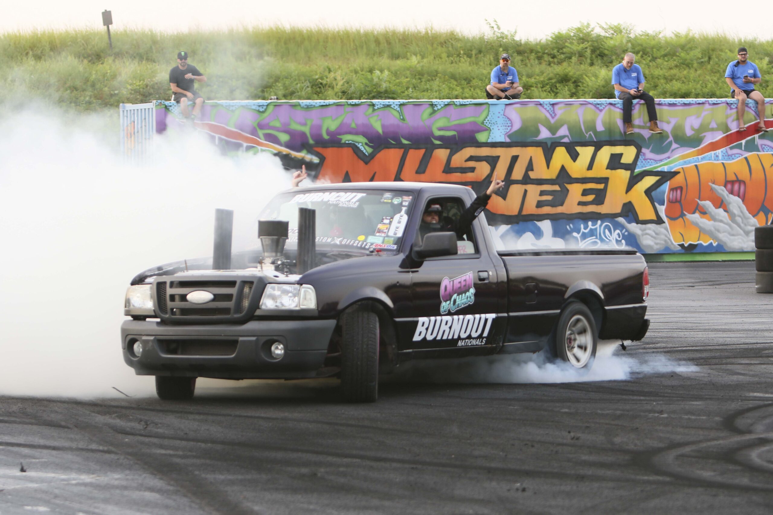 Black pickup truck performing burnout at Mustang Week event.