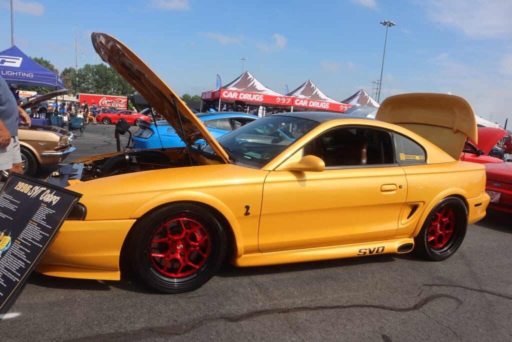 Gold Ford Mustang with red wheels at Mustang Week event in Charlotte.
