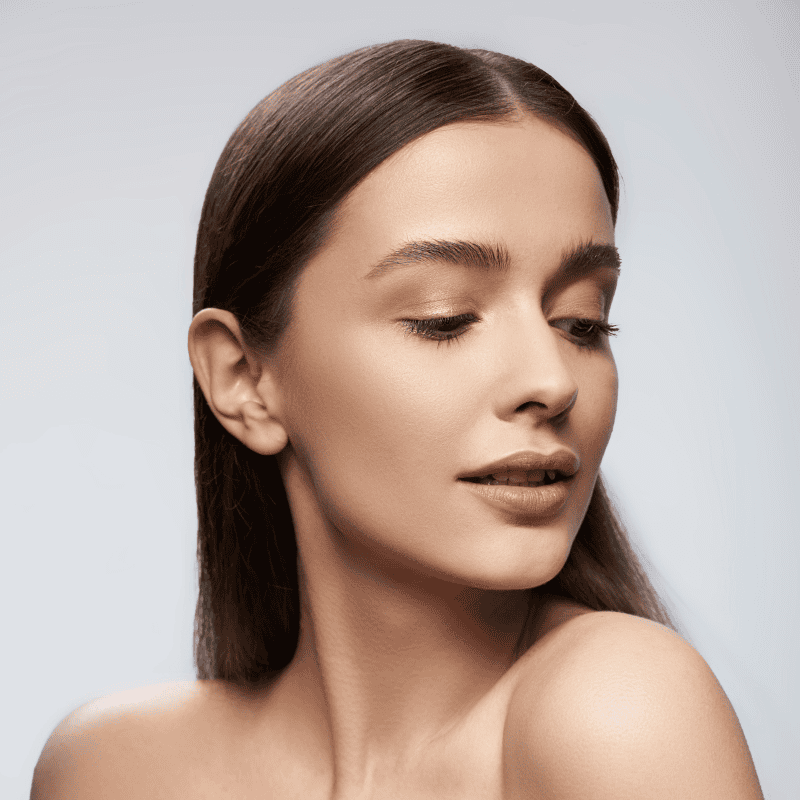a women sitting in a chari wearing a robe looking at herself in the mirror with her right hand on her face