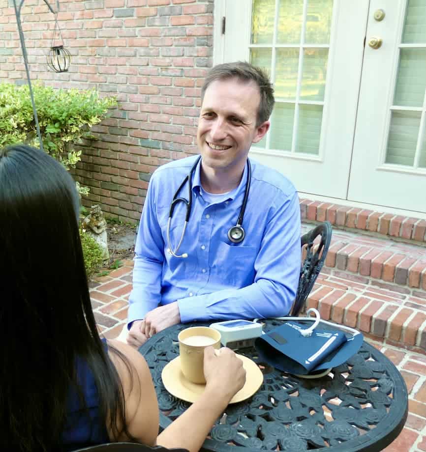 two men sit on a bench talking looking a tablet