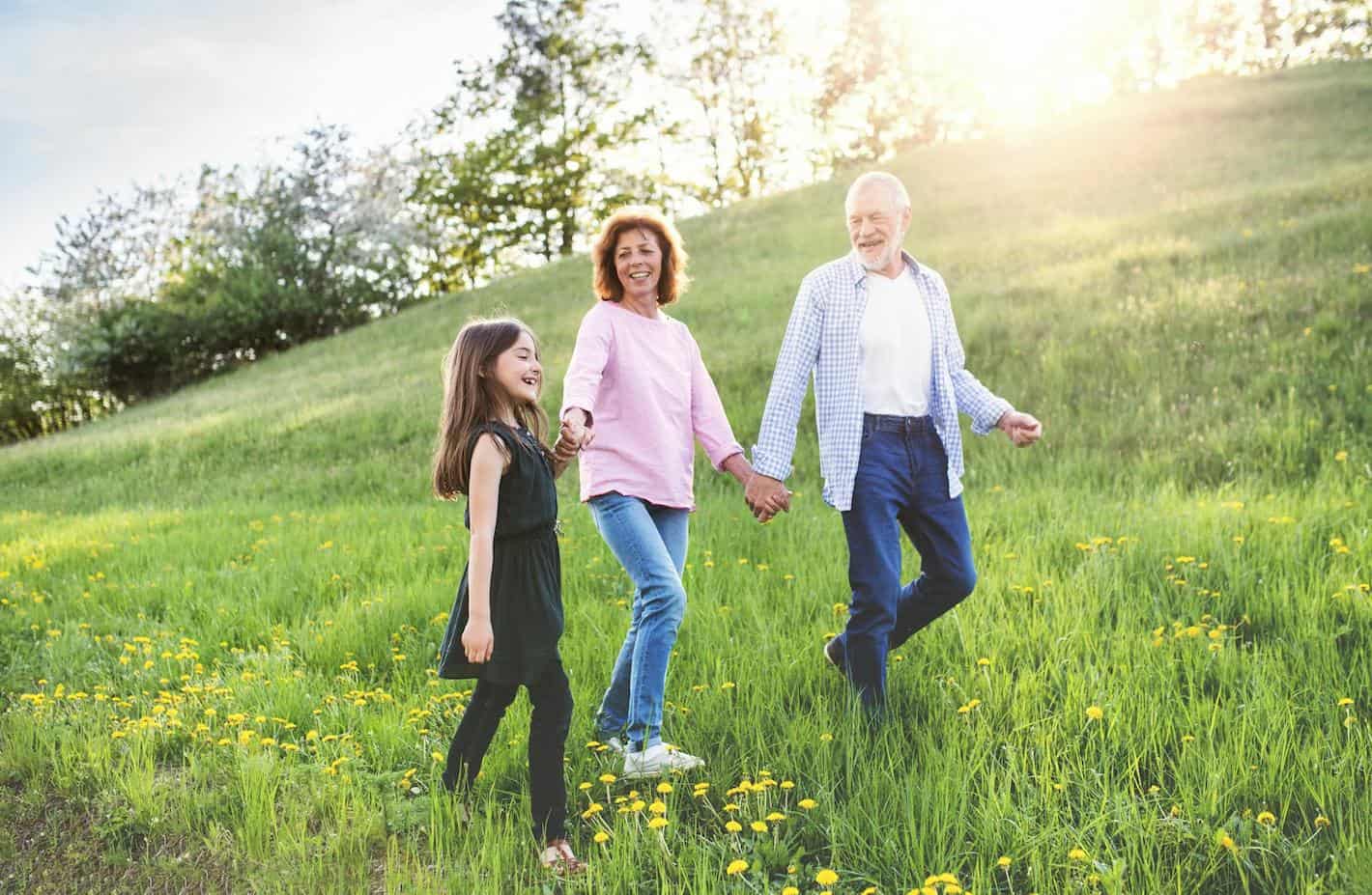 an older couple walking with their granddaughter on a hill with the sun shinning
