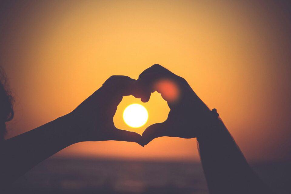 two hands holding a heart over the sun