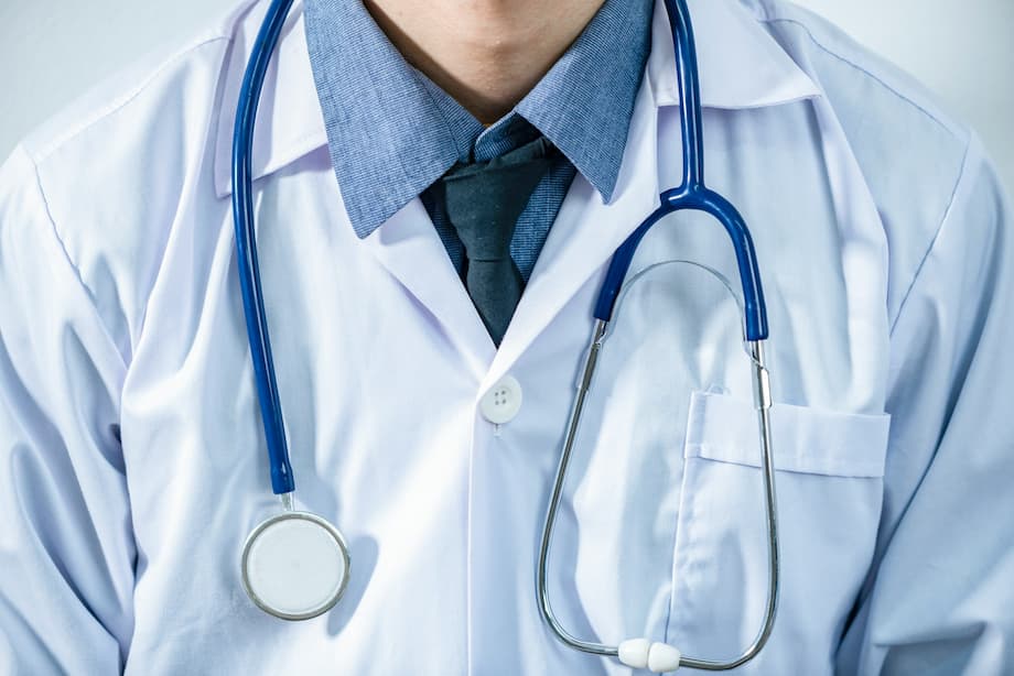 Doctor standing wearinga  white coat with a blue stethescope around his neck