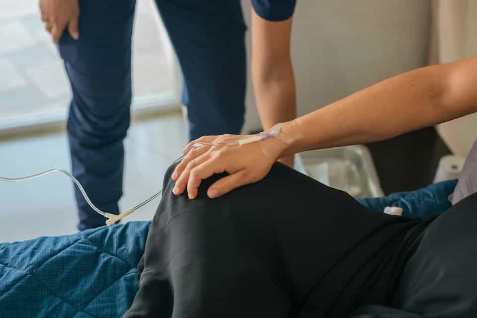 a woman sitting on a bed with an IV in her right forearm