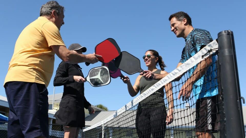 4 people standing around a net holding their pickleball racket