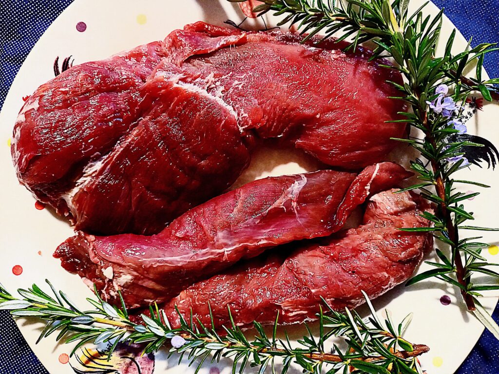 Venison loin and fillet on a white plate with rosemary sprigs