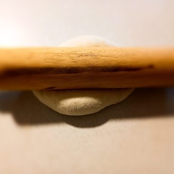 rolling pin on top of pizza dough on a cream colored bench top