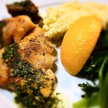trout crispy skin with mash potatoes, lemon wedge and broccolini on a white plate