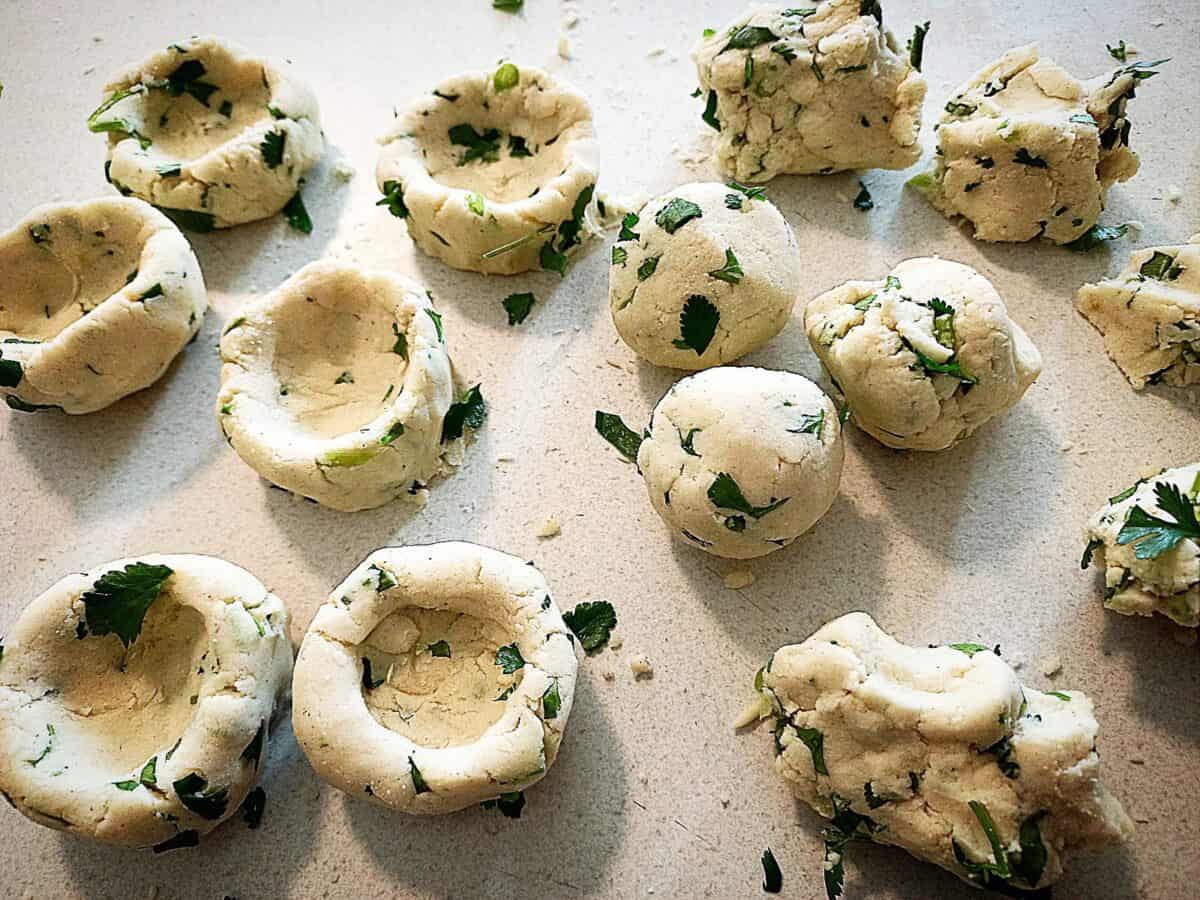 Making masa corn and coriander dumplings. On a cream colored bench top are 6 Chochoyotes and 6 Masa corn dough balls being formed