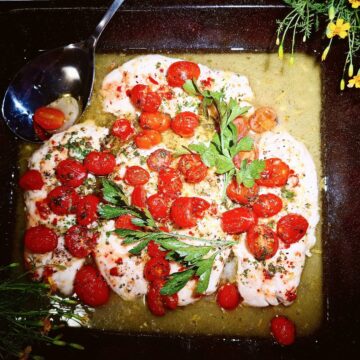 Baked cod with lemon, parsley, tomatoes and white wine in an oven tray.