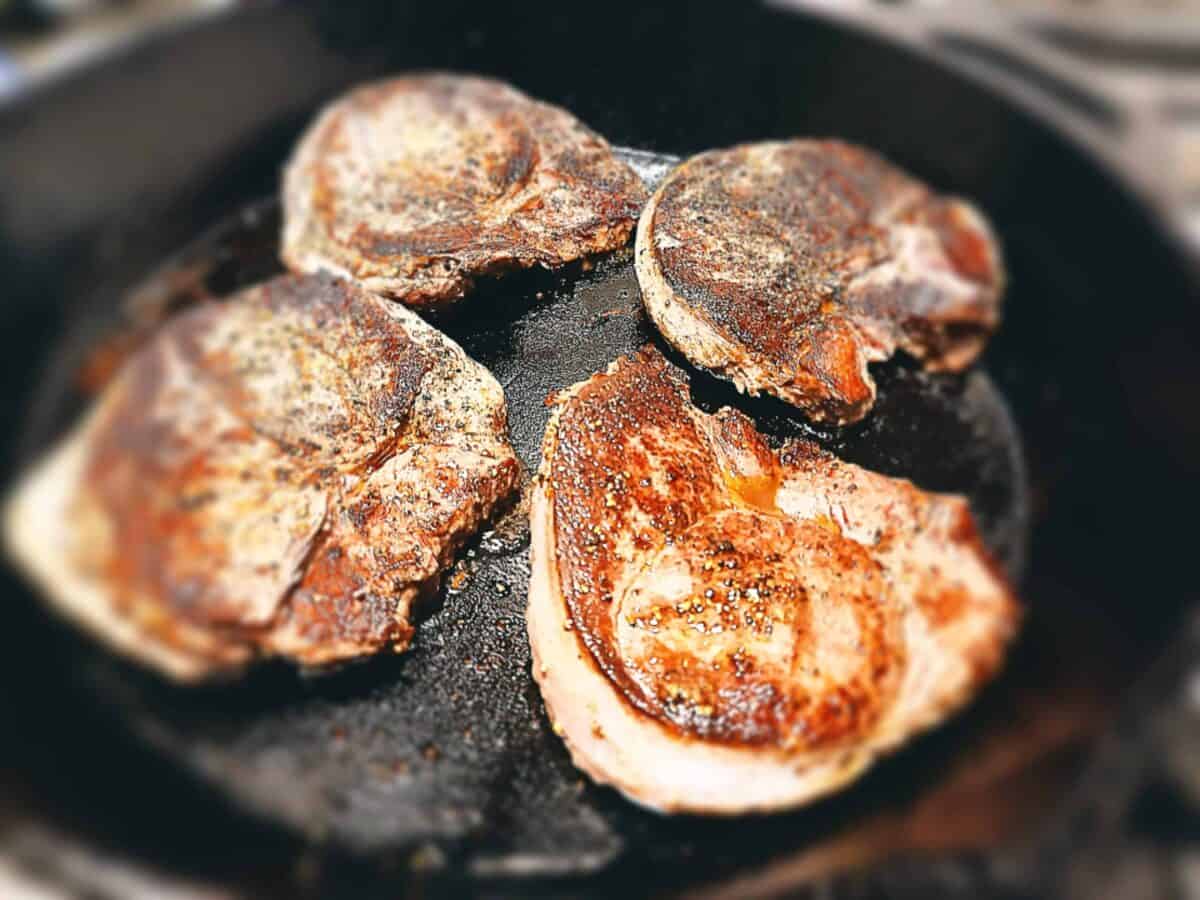 Venison steaks cooking in a cast iron skillet pan