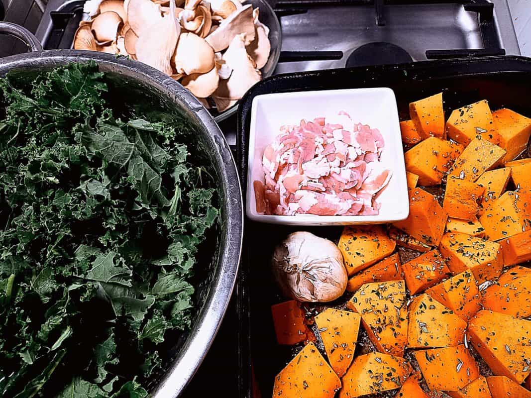 Bacon, cut pumpkin, cut kale a garlic head and oyster mushrooms layd out for making roast vegetable gnocchi