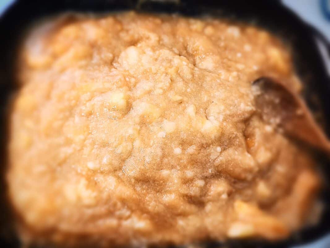 Applesauce compote cooking in a large square sauce pan. A wooden spoon stirring the sauce