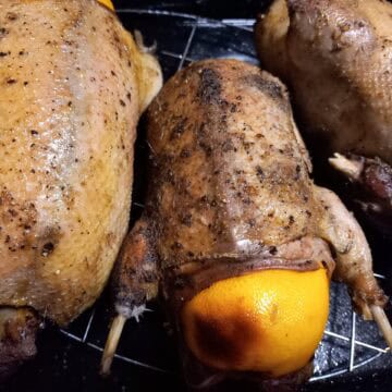3 roasted wild ducks on an oven rack. The middle one has a whole orange in the cavity. Half of the orange is sticking out