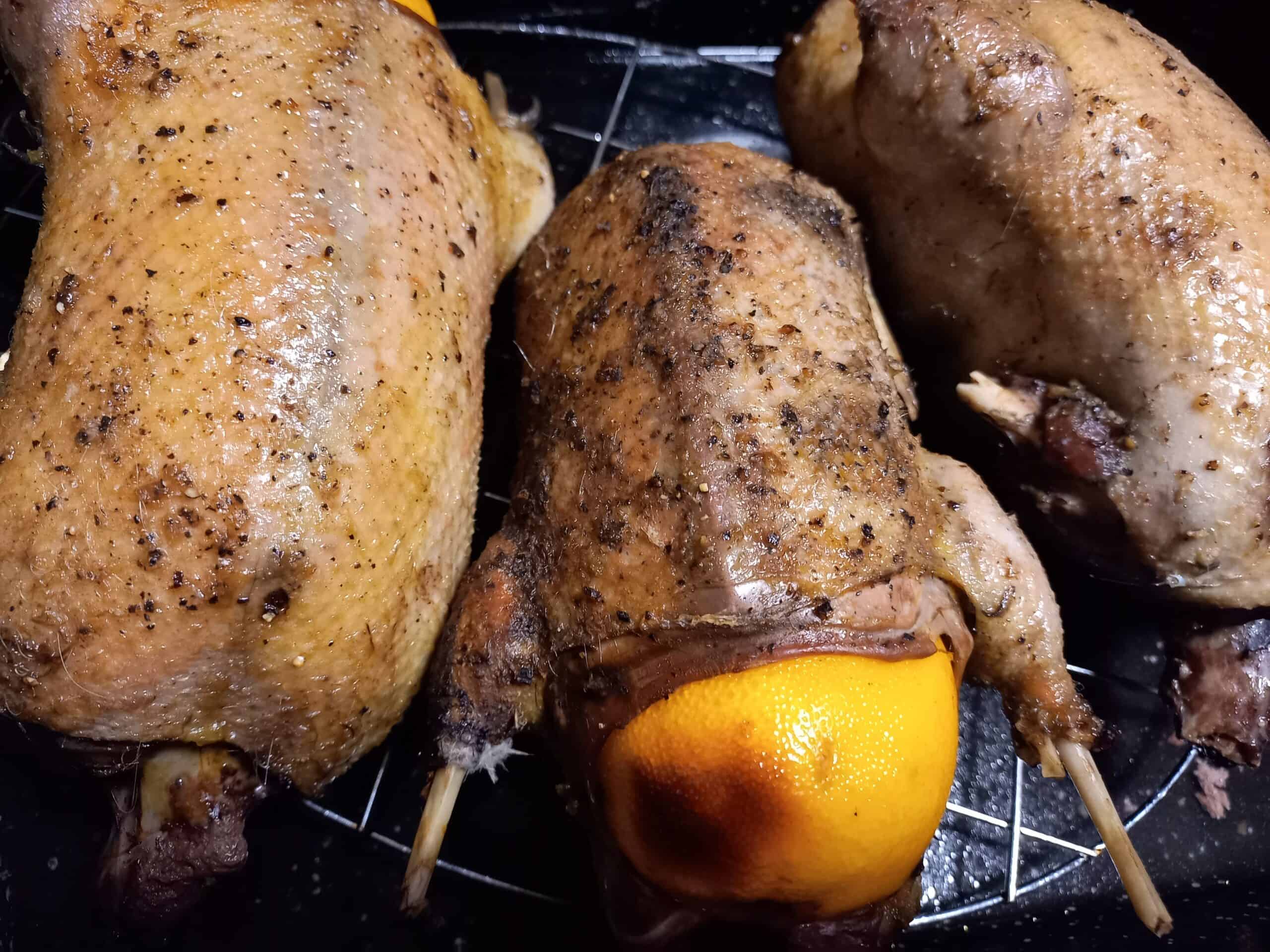 3 roasted wild ducks on an oven rack. The middle one has a whole orange in the cavity. Half of the orange is sticking out